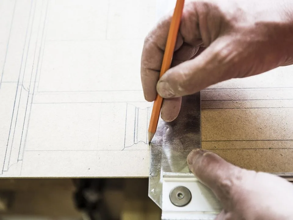 Hände zeichnen mit Bleistift und Anschlagwinkel eine Linie auf eine Holzplatte