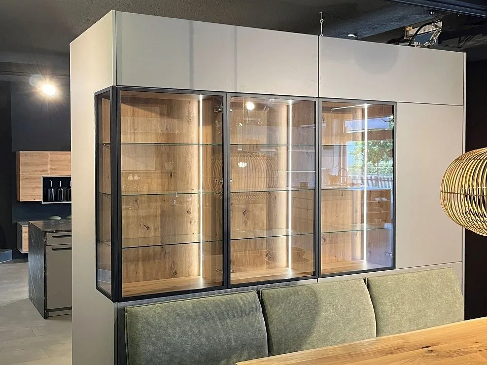 Beleuchtete Glasvitrine mit Holz-Innenleben über einer grünen Sitzbank