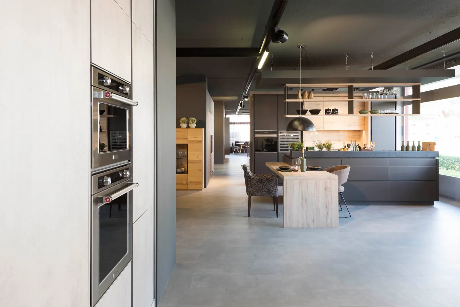 Blick durch den Showroom an Backöfen vorbei auf eine dunkle Kochinsel mit Hängeregal