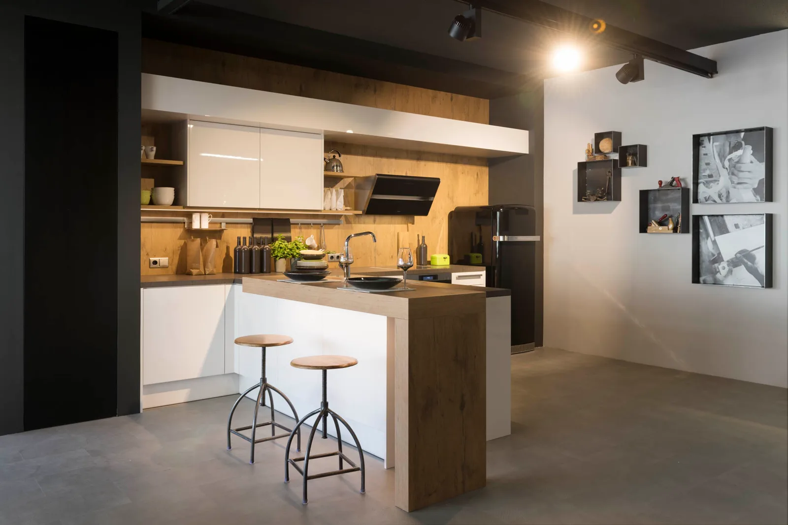 Weiße Küche im Showroom mit Holzrückwand, Theke und zwei Barhockern